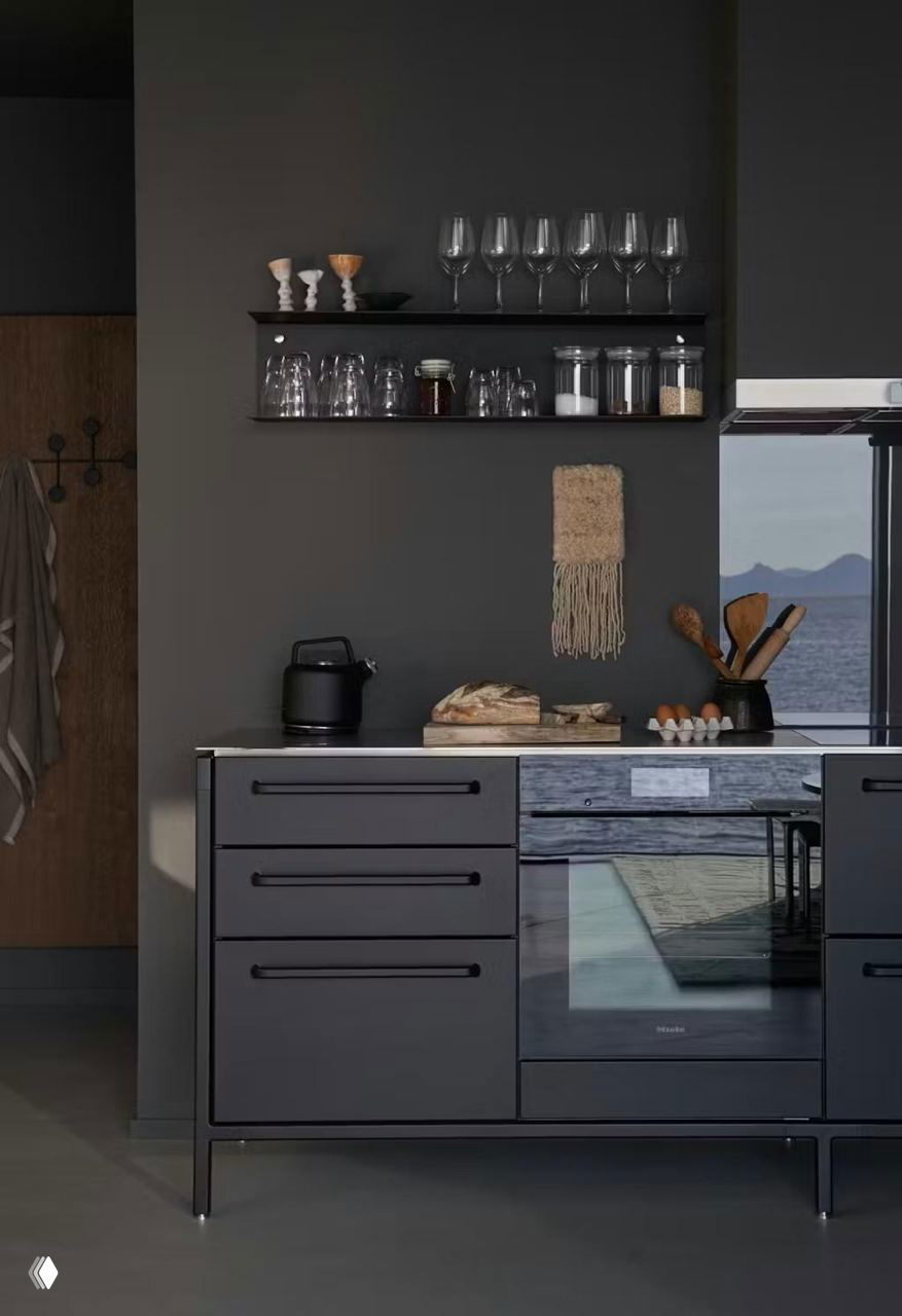 Кухонный уголок в тёмных натуральных тонах: минималистичные фасады, открытые полки с посудой и окно с видом на морской горизонт.