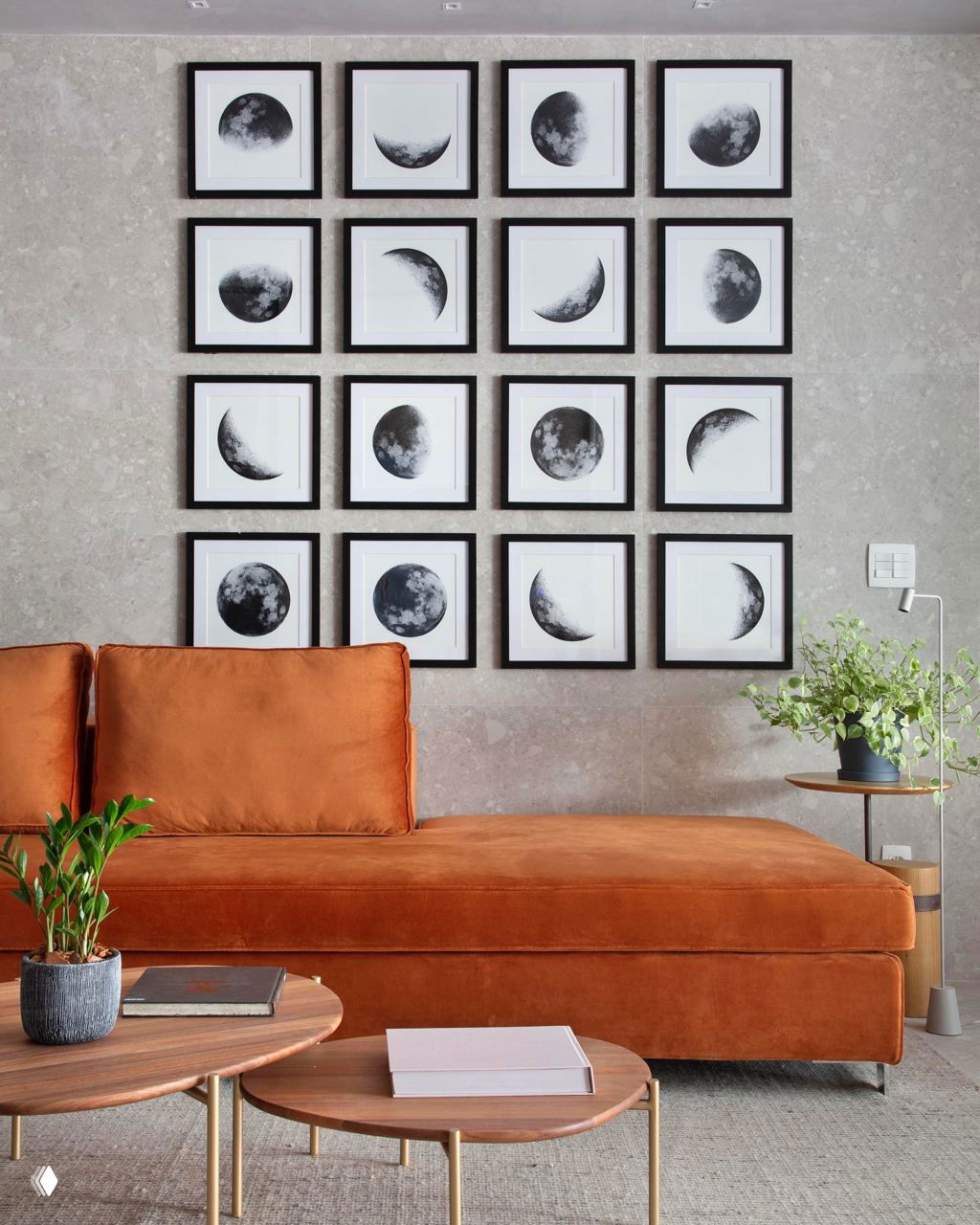 Уютная зона с диваном насыщенного хурмово-оранжевого цвета на фоне сетки рам с изображением фаз луны, кофейные столики и растения добавляют фактуры.