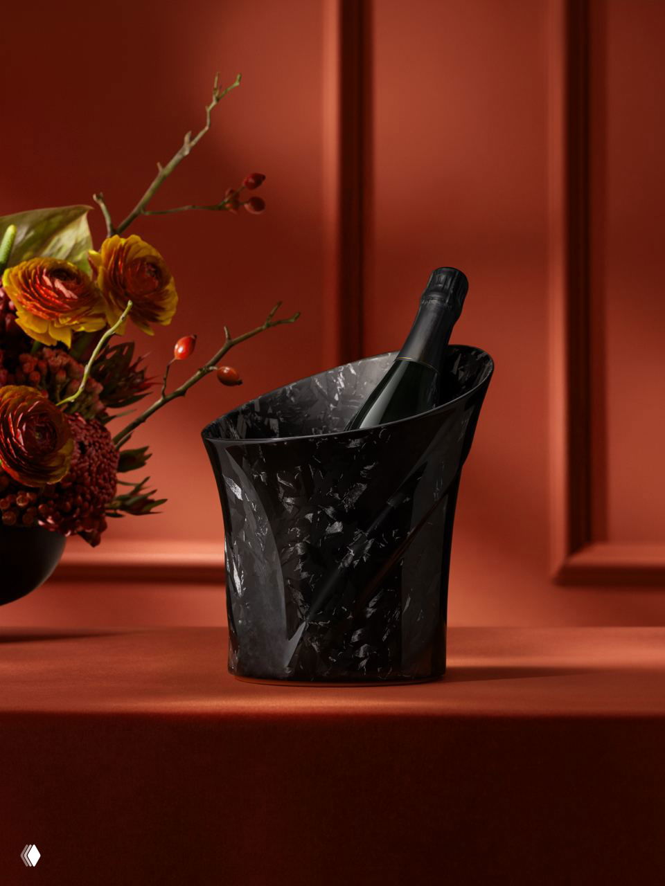 Черный винный кулер из кованого карбона на тёплом красном фоне с бутылкой шампанского и декоративной цветочной композицией.