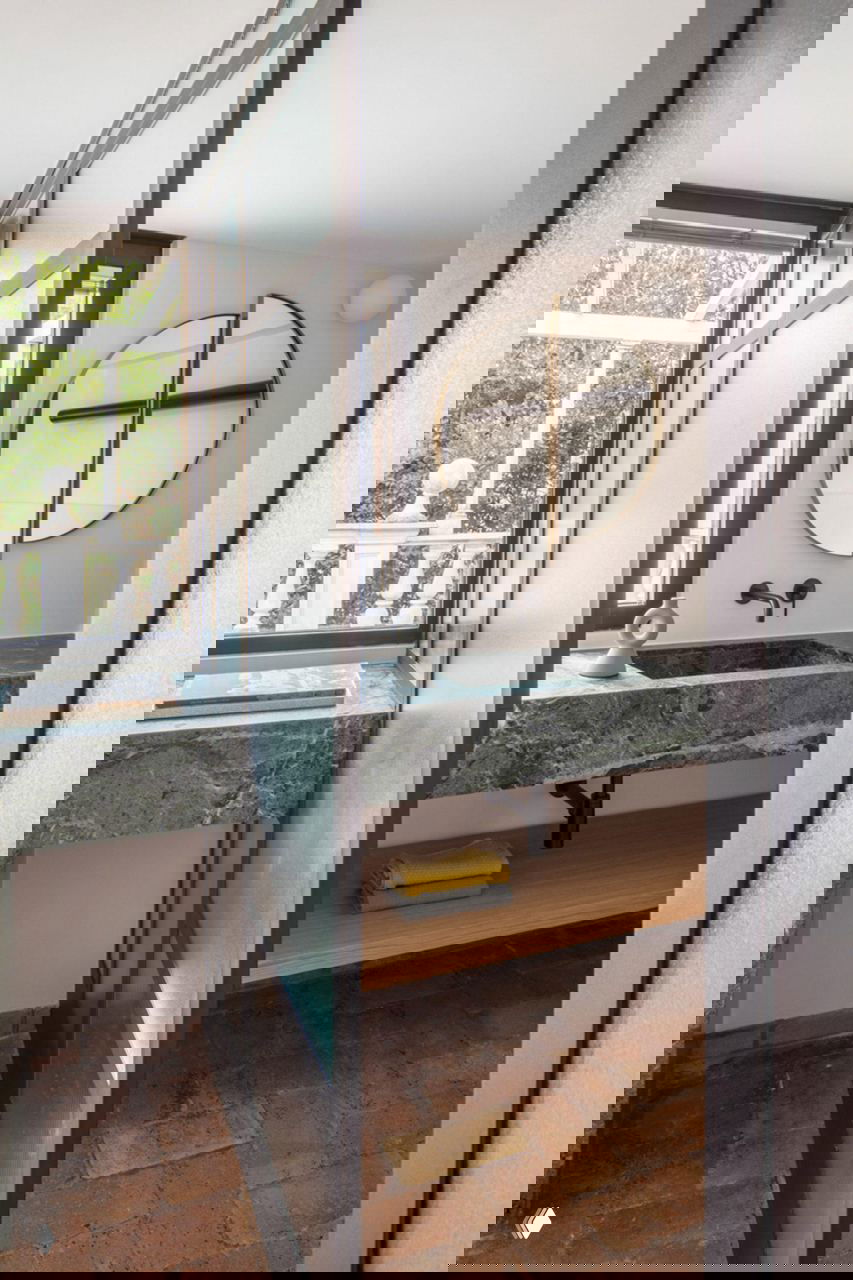 Интерьер ванной и умывальника: зелёный мраморный подоконник‑раковина, круглое зеркало и мягкое дневное освещение с видом на балкон.