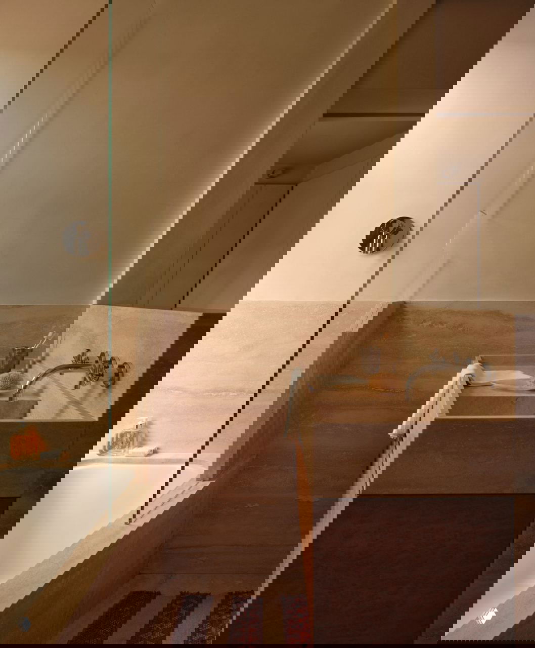 Ванная комната в бежевых тонах: ванна с стеклянной перегородкой, встроенная каменная раковина и деревянная тумба — лаконичная отделка.