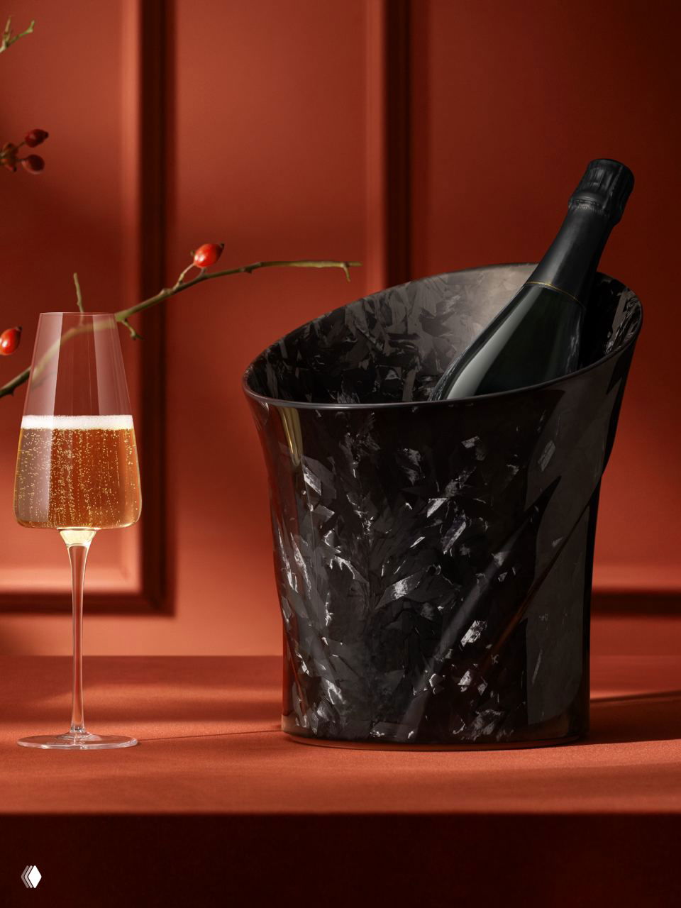 Крупный план черного кулера из кованого карбона с бутылкой внутри и бокалом игристого вина на фоне бархатисто-красной стены.