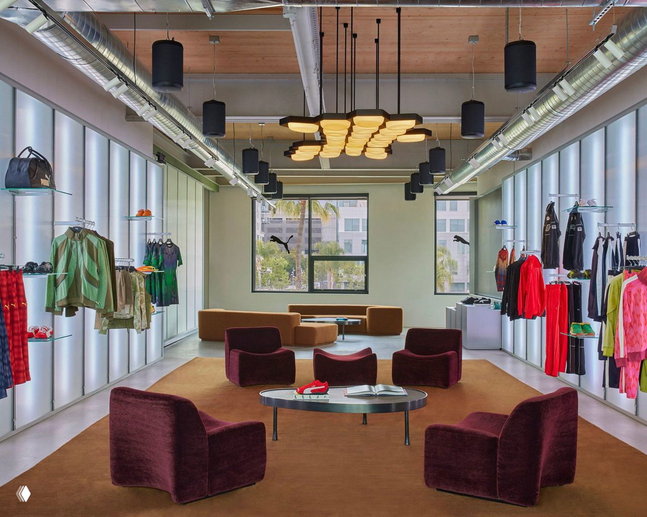 Шоурум Puma Studios: просторное помещение с выставочными стеллажами, мягкими креслами, витринами с одеждой и видом на город через большое окно.