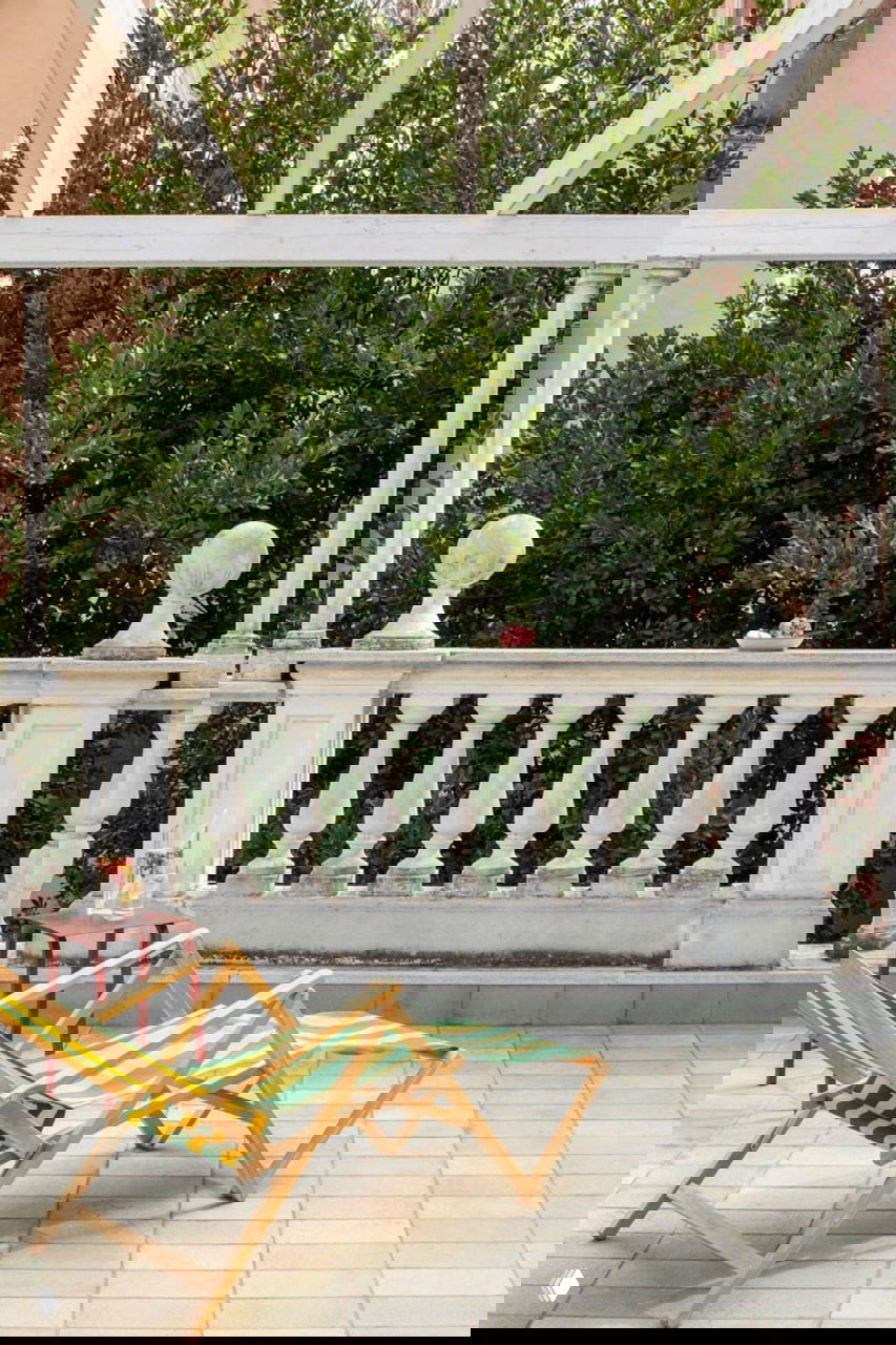 Живописная терраса с классической балюстрадой, шезлонгами в полосатой ткани и зелёными насаждениями на фоне пастельных фасадов Рима.