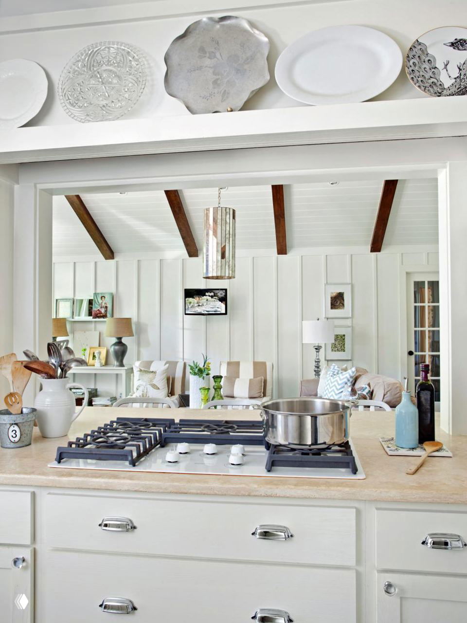 Кухонная столешница с варочной панелью на переднем плане и широким проёмом в гостиную — пример объединённой зоны через окно‑проём