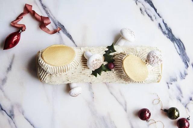 Рождественское полено на мраморной поверхности, украшено мини-орнаментами и новогодней сервировкой, вид сбоку.