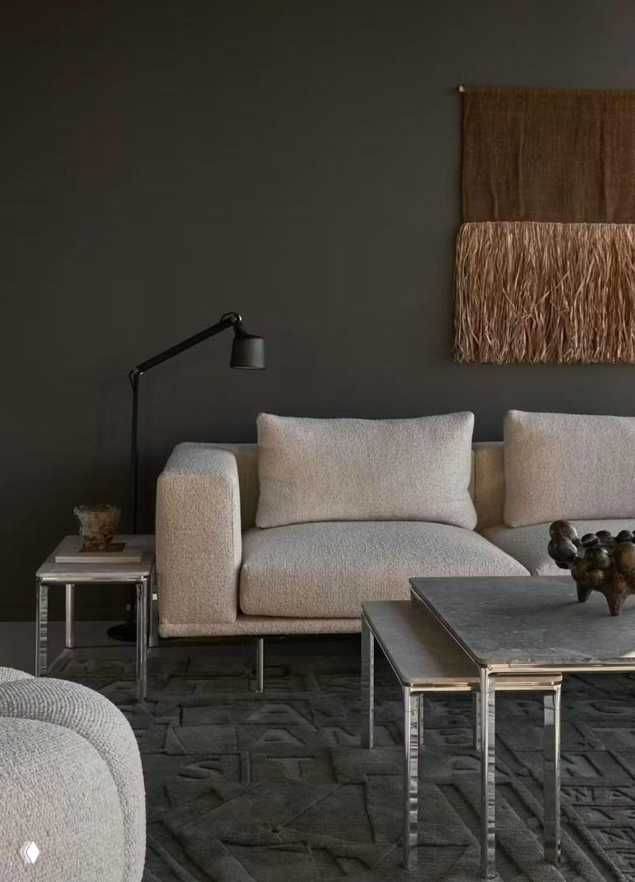 Гостиная зона с бежевым диваном, низкими столиками и текстильной панелью на тёмной стене — тёплый фактурный интерьер в скандинавском ключе.