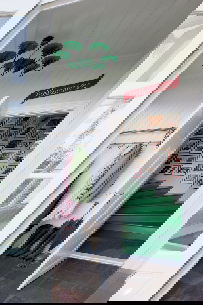 Прихожая с открытой дверью, зелёной лестницей, вешалкой с верхней одеждой и стеной, уставленной рамками с семейными фотографиями — традиционный шведский дом.