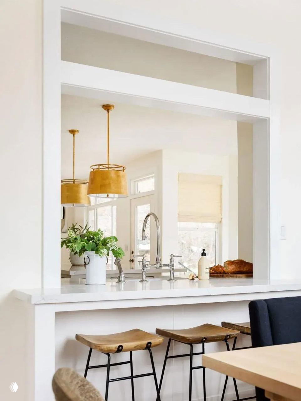 Широкий прямоугольный проём‑окно между кухней и столовой, светлая столешница и три деревянных табурета у барной стойки