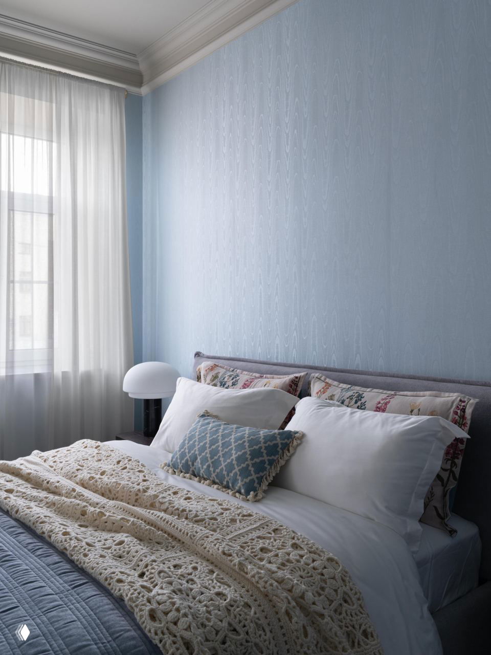 Спальня с небесно-голубыми стенами, аккуратно заправленной кроватью, вязаным пледом и декоративными подушками в спокойной текстильной гамме.