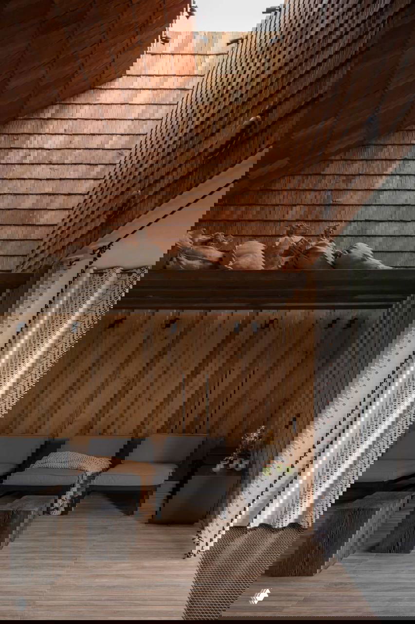 Интерьер бани или лаунж-зоны с высокими деревянными стенами и черепичной обшивкой, зона отдыха с шезлонгами и мягкими текстурами.