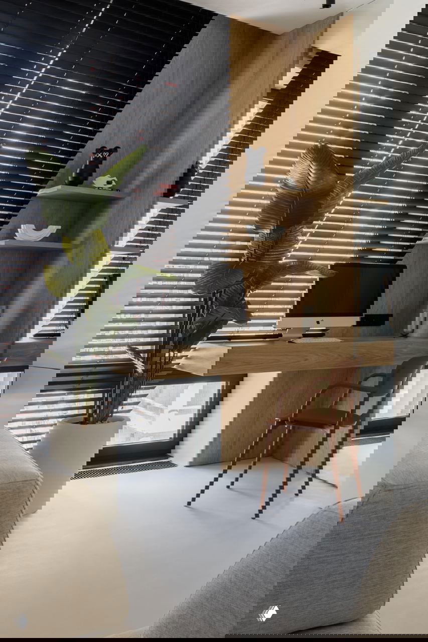 Рабочая зона у окна: настенный деревянный стол, компьютер iMac, зеркальная панель, высокая зелёная декоративная пальма и чёрные горизонтальные жалюзи на окне.