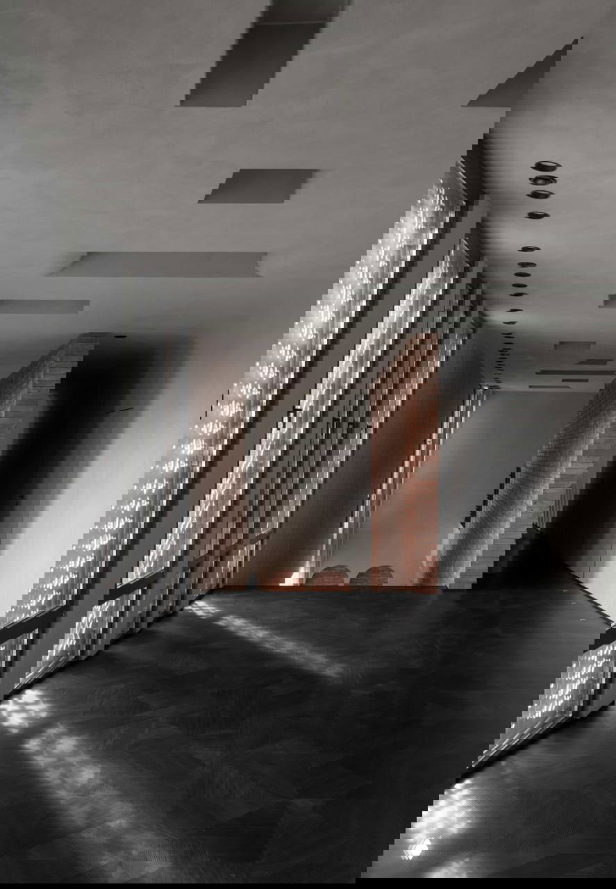 Длинный светлый коридор с декоративными решётками на окнах, чёрным паркетом и мягким светом, создающим узоры на полу и стенах.