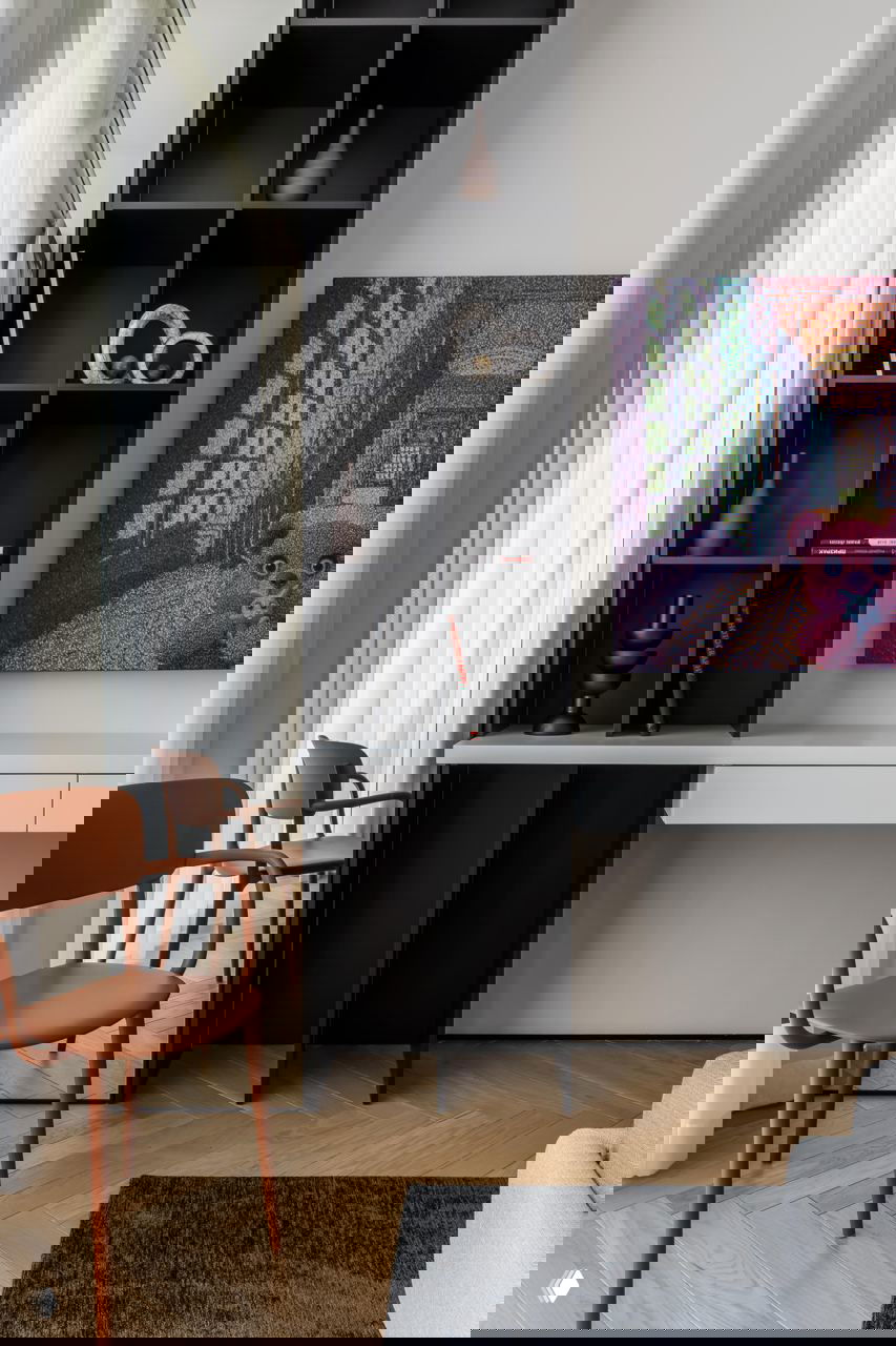 Ниша с рабочим столом и открытой чёрной стеллажной системой, белая столешница, декоративные предметы и яркая картинная композиция как акцент в комнате.