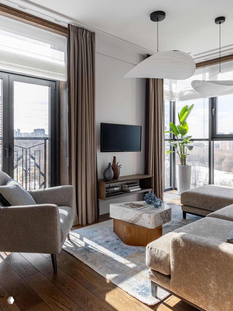 Комната с двумя окнами, тёмными шторами и синим диваном, оригинальный прозрачный журнальный столик и приглушённая художественная палитра.