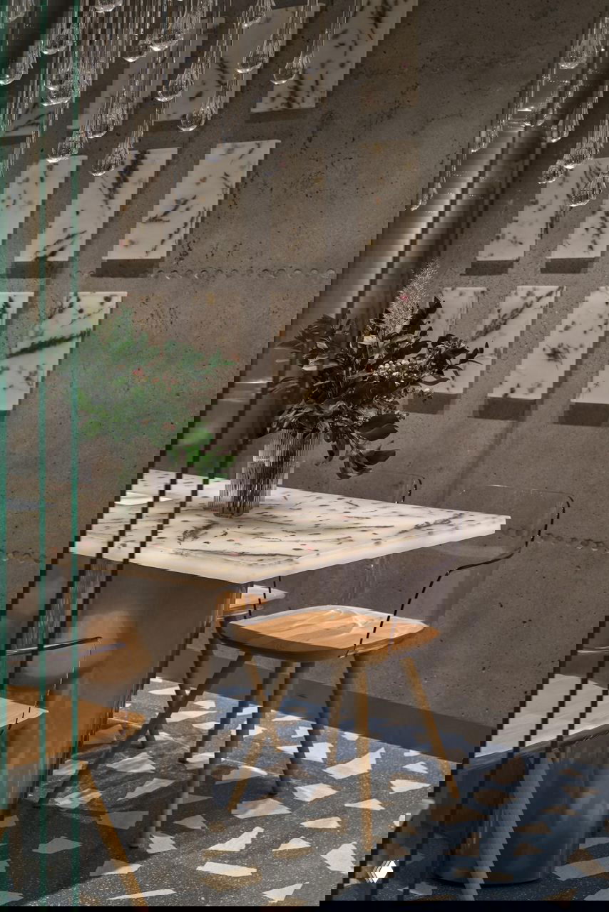 Стол с мрамороподобной столешницей в стиле терраццо и прозрачные стулья на фоне бетонной стены с декоративными панно; интимная зона ресторана.