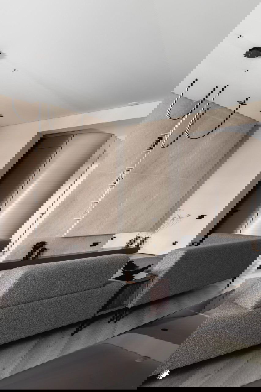 Гостиная в тёплом минимализме: низкие серые диваны, светлая декоративная стена с нишей, лаконичные подвесные светильники и паркет ёлочкой в проекте Жанны Бондаренко.