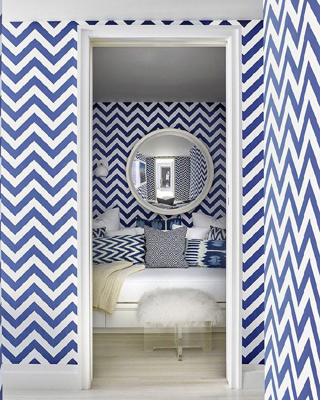 Яркая зона с зигзагообразным синим принтом на стенах и уютным небольшим диваном‑спальным местом, круглое зеркало создаёт глубину помещения.