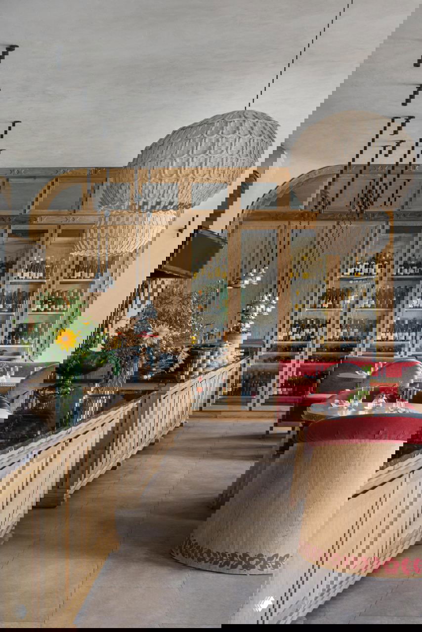 Барная зона и винный шкаф: тёплая деревянная отделка, барная стойка с чёрной столешницей, стеклянные витрины с бутылками и уютные места для гостей.