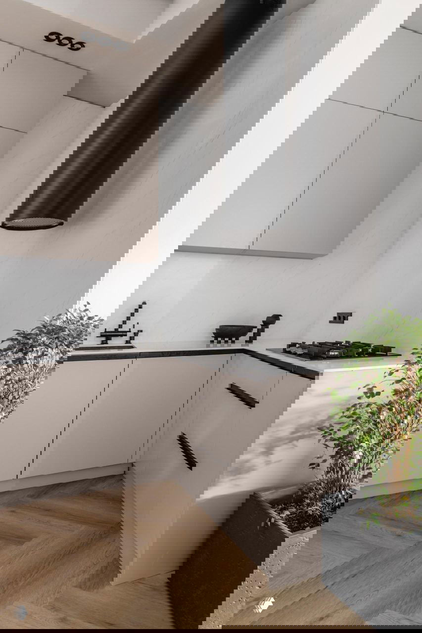 Кухонный уголок с бежевыми фасадами, чёрной вытяжкой и варочной панелью, черными аксессуарами и растением на подоконнике в проекте Жанны Бондаренко.