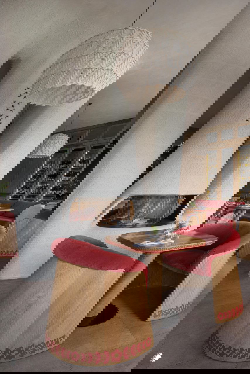 Каминная зона с белыми скульптурными колоннами и округлыми каминами, рядом деревянные кресла с бархатной красной обивкой и фольклорным орнаментом по низу.