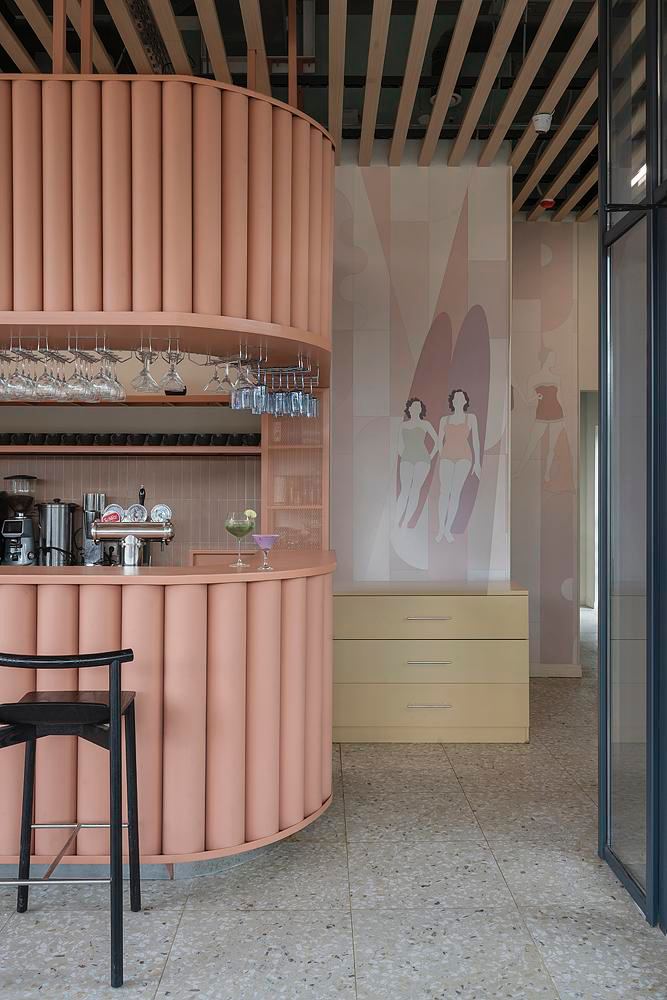 Крупный фрагмент изогнутой барной стойки и настенной росписи с силуэтами людей в плавках — пастельные тона и мягкая фактура материалов в интерьере.