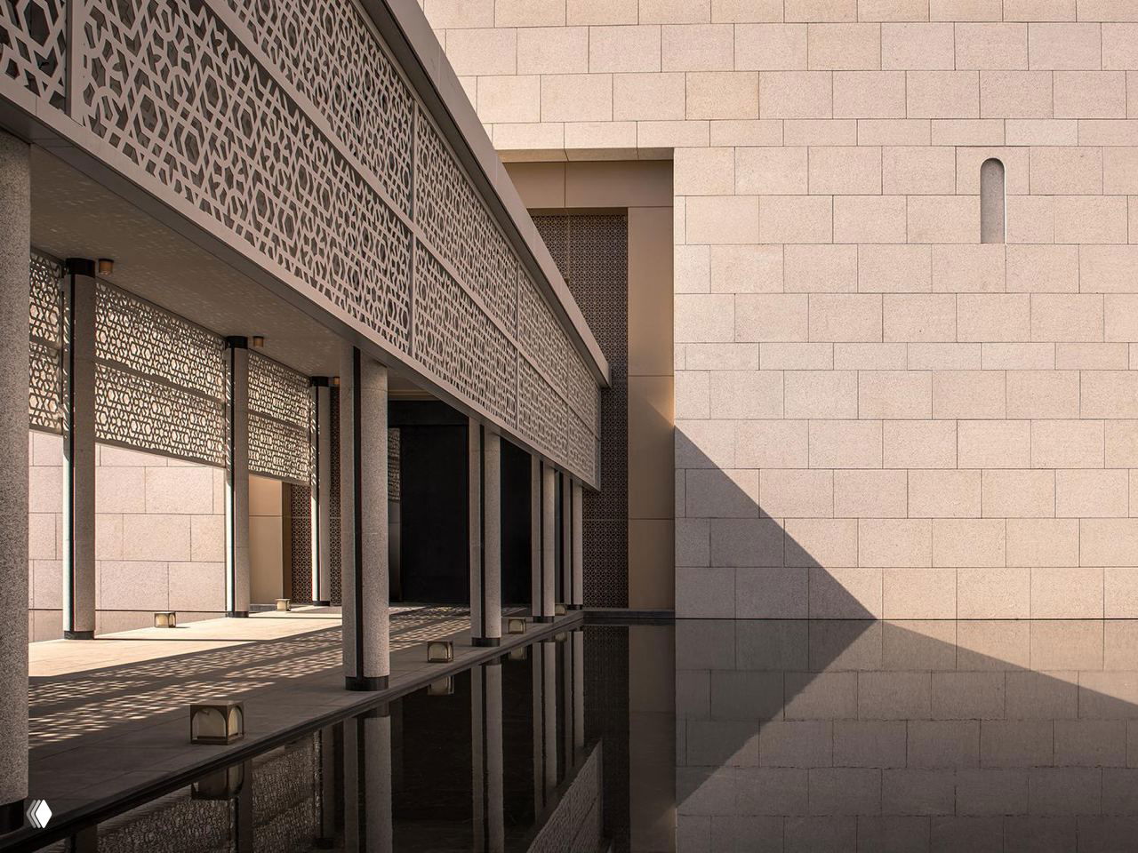 Переход с ажурными резными панелями и колоннами, теневая игра на стенах и спокойная водная гладь — деталь экстерьера отеля в концепции, вдохновлённой Шёлковым путём.