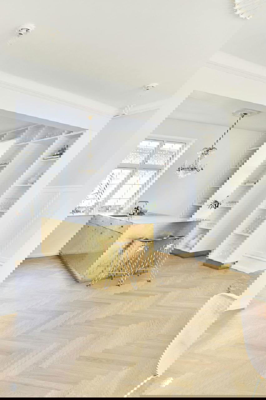 Кухонная зона с позолоченным латунным островом, барными стульями и хрустальной люстрой — сочетание классики и современного декора.