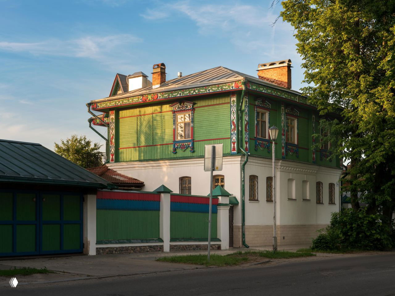 Деревянный расписной дом с зелёными ставнями и цветной отделкой на тихой улице Суздаля, отражающий традиционный местный стиль оформлений фасадов.