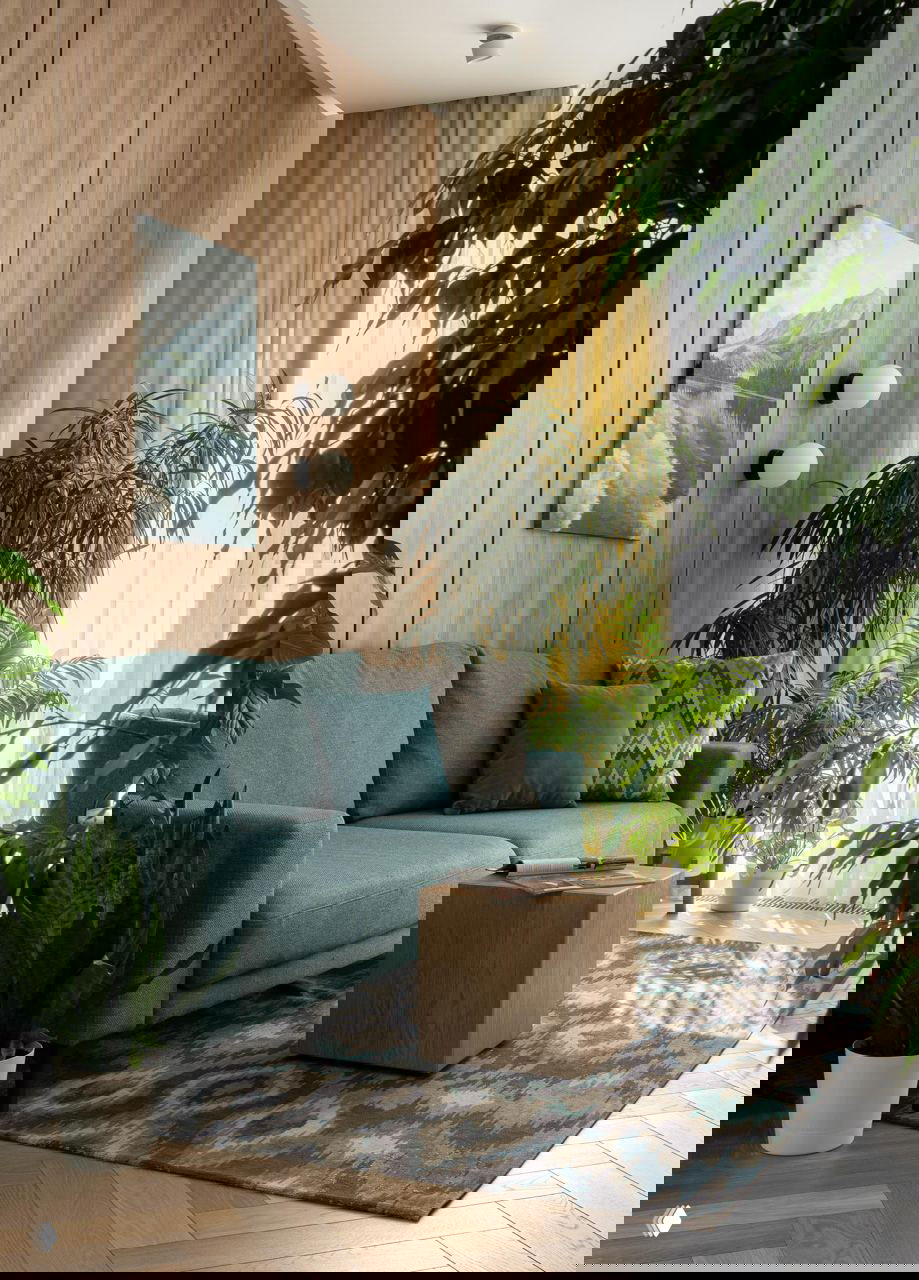 Гостиная с бирюзовым диваном, деревянной стеновой панелью и множеством зелёных комнатных растений у окна при мягком дневном свете.