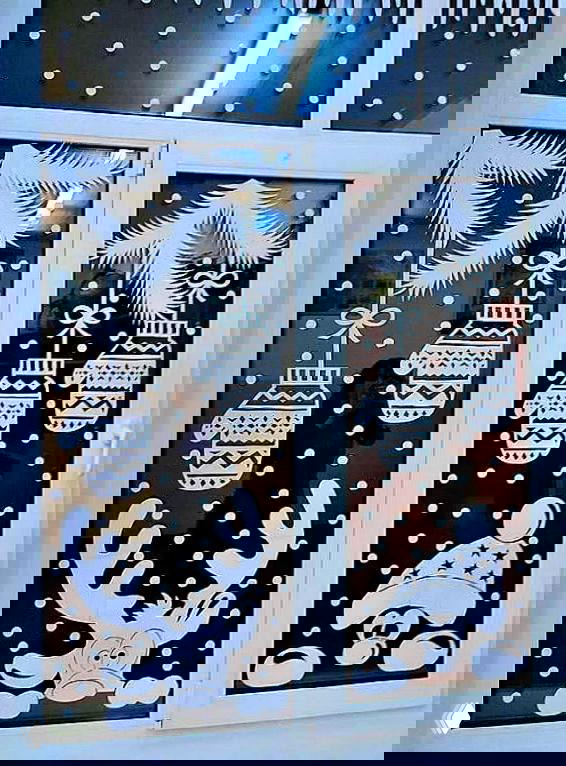 Новогодняя вытынанка на окне: подвесные игрушки, олень и медвежонок, снежинки и гирлянды на тёмном фоне — сезонный бумажный декор.