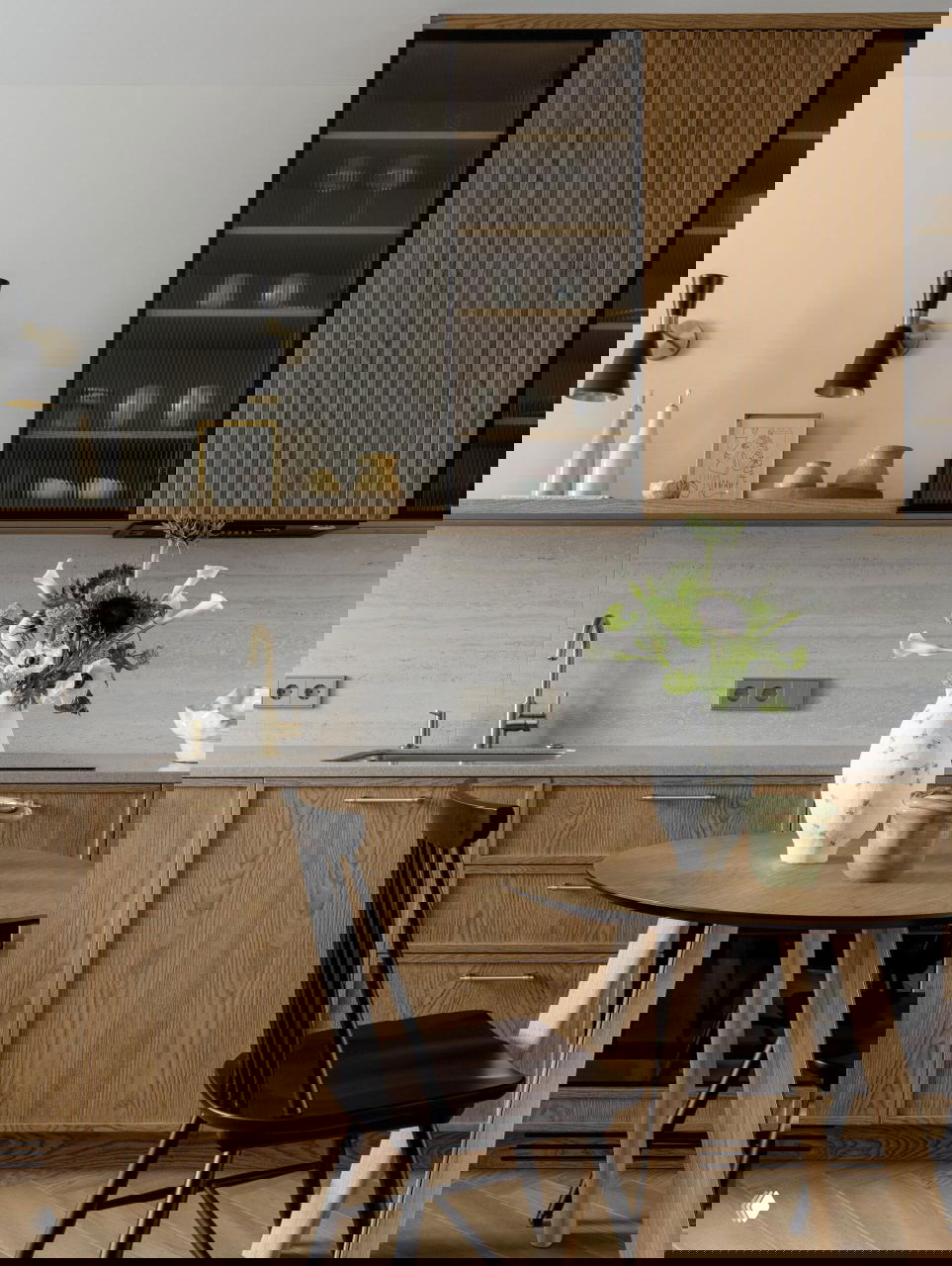 Кухонная зона крупным планом: стол с вазой, латунный смеситель, деревянные шкафы и текстура натуральных материалов в интерьере.