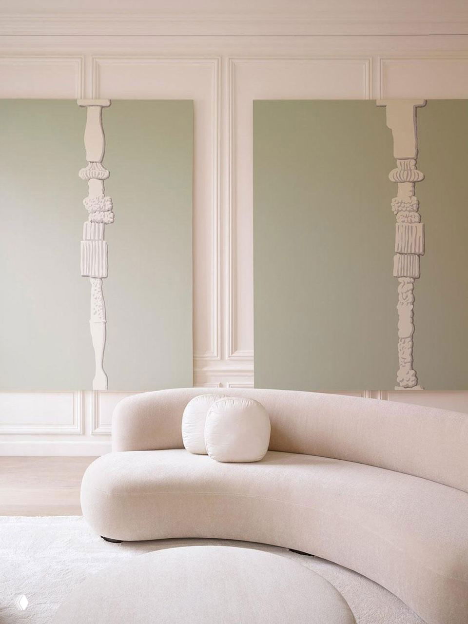Светлая монохромная зона отдыха: изогнутый бежевый диван на фоне пастельно-зеленых панелей и минималистичных рельефов на стене.