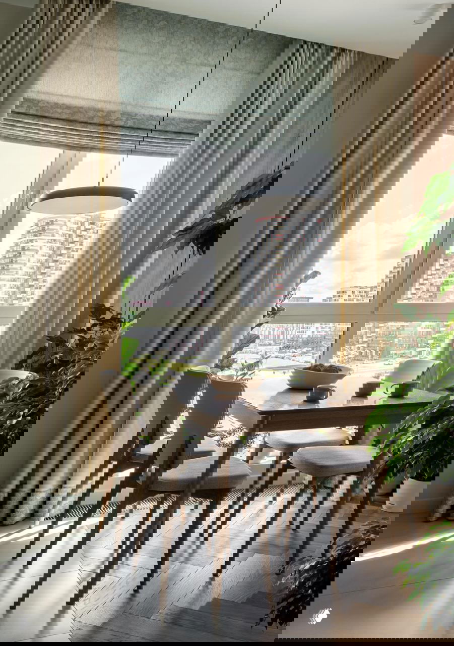 Обеденная зона у большого окна: деревянный стол, шторы нейтрального тона и растения на подоконнике с видом на городской квартал Минска.