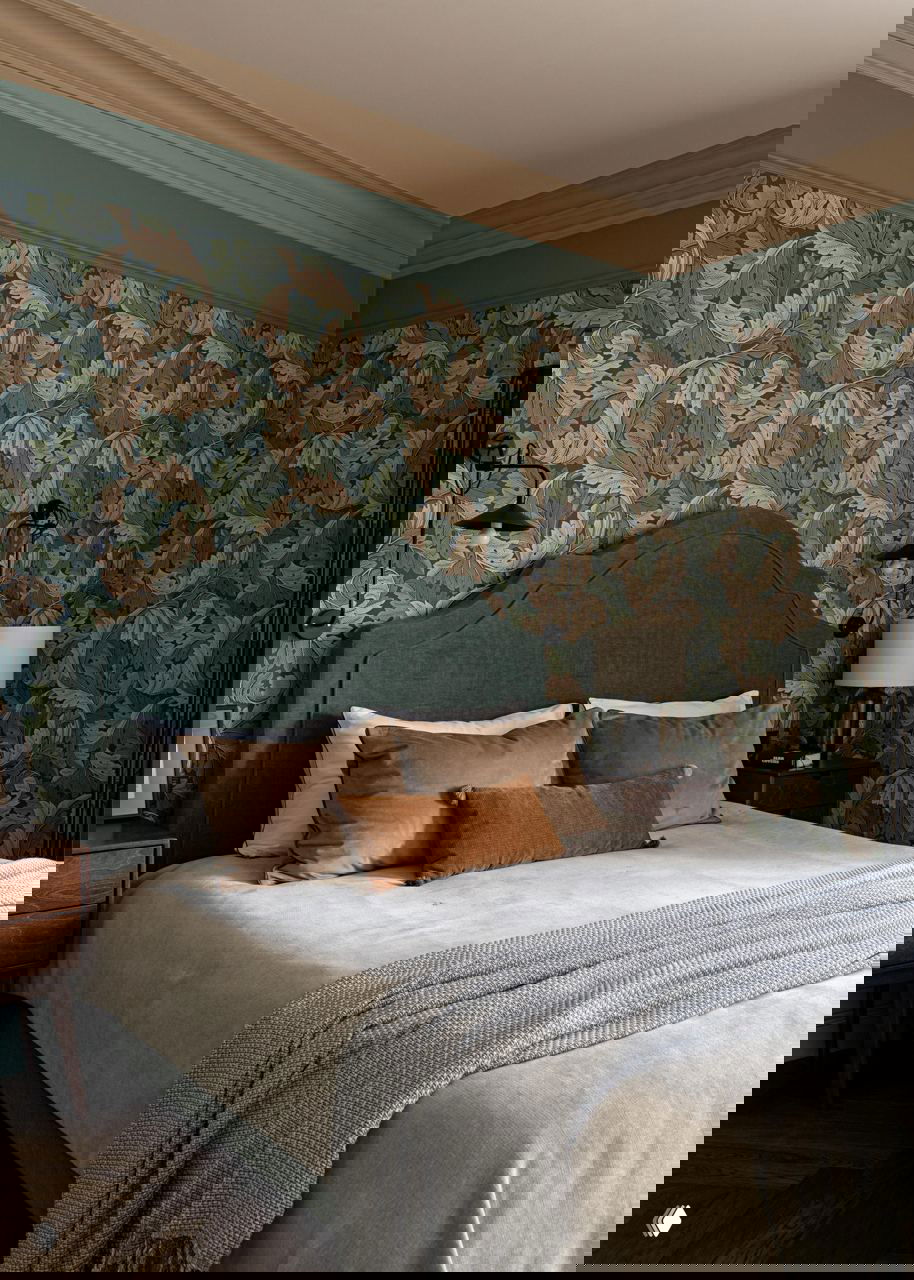 Спальня с обивкой из зелёной ткани, роскошными обоями Morris &amp; Co в растительном орнаменте, мягкими бархатными подушками и деревянными тумбочками.