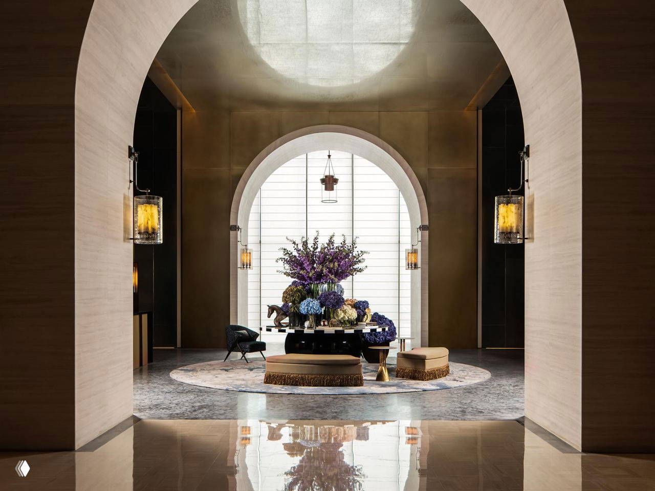 Арочный вход в лобби с бронзовыми светильниками и богатой цветочной композицией в центре — сочетание традиционных декоративных приёмов и современного минимализма интерьера.