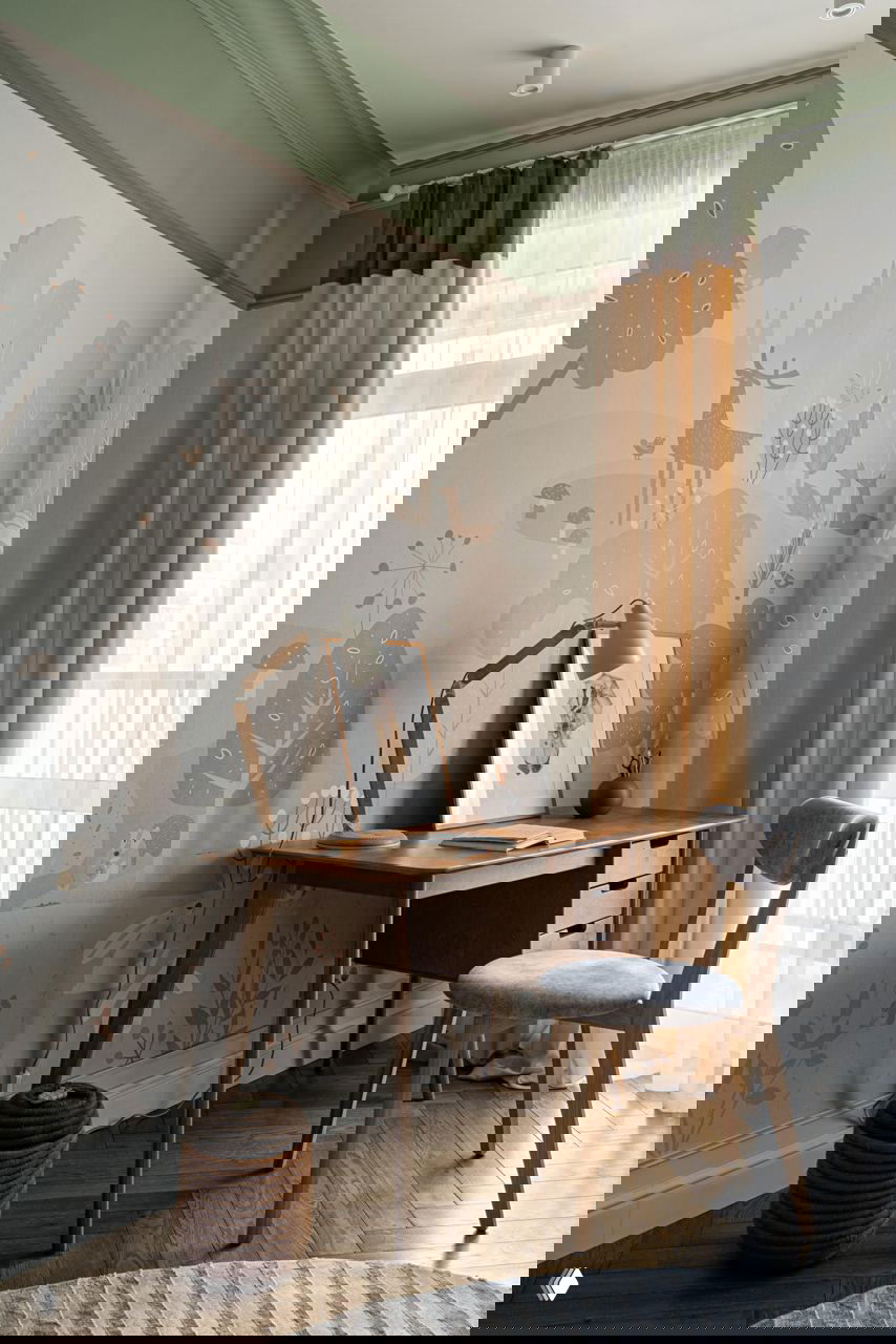 Рабочий уголок в детской/кабинете: письменный стол, стул, занавеси в тёплых тонах и обои с иллюстративным лесным принтом с животными и растениями.