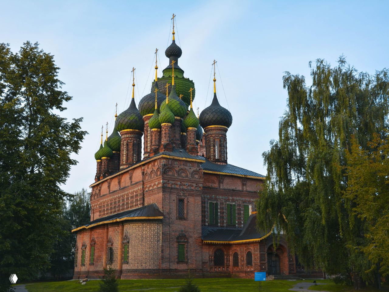 Кирпичная церковь с зелёными луковичными куполами на фоне неба, окружённая деревьями — архитектурный исторический памятник Ярославля.