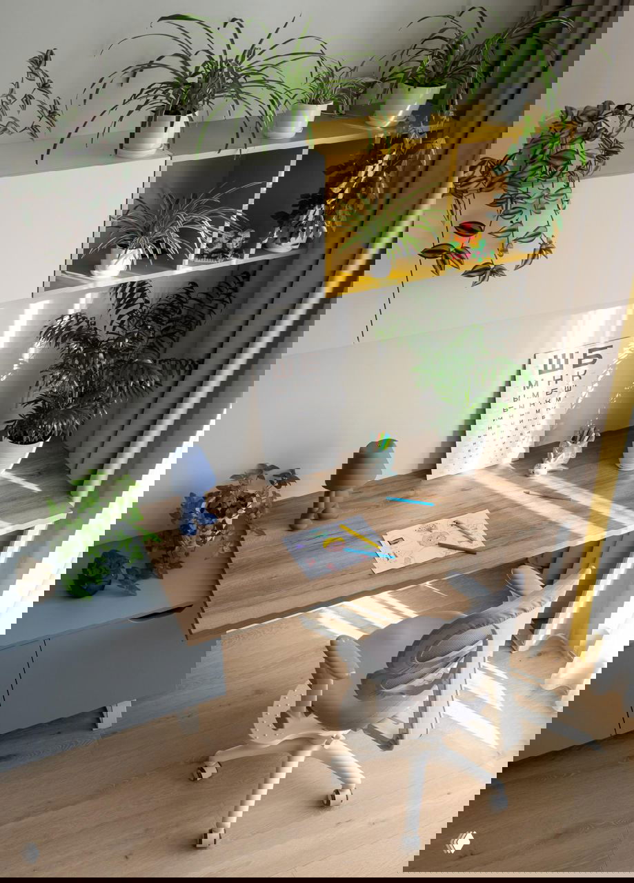 Детский рабочий уголок с деревянным столом, эргономичным креслом и растениями на полках — светлая зона для учебы и творчества ребёнка.