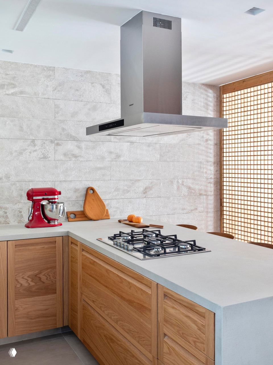 Угловая кухня с рабочим полуостровом, встраиваемой варочной панелью и крупной островной вытяжкой на фоне текстурной светлой стены и деревянных фасадов.