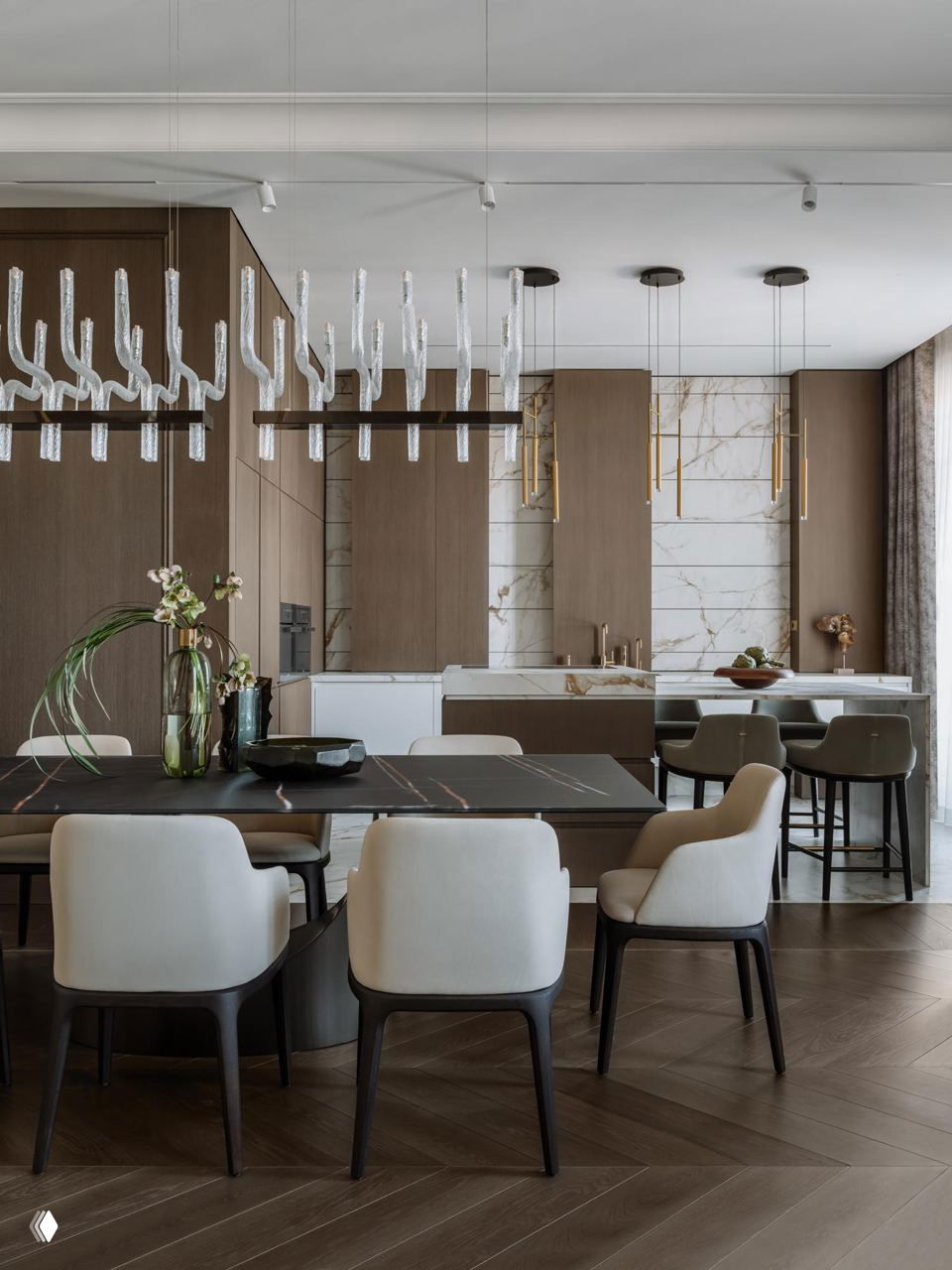 Общая зона столовой и кухни: тёмный обеденный стол, белые стулья, деревянные фасады кухни, мраморные фартуки и подвесные латунные светильники над столом.