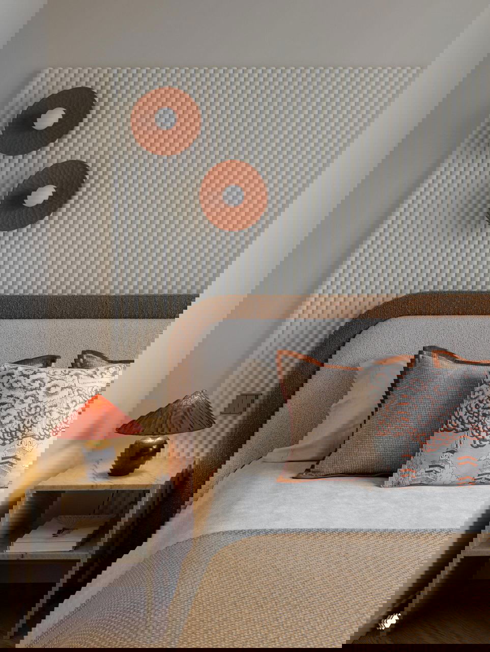 Спальня с изголовьем в нейтральной текстуре, декоративными круглыми элементами на стене и спокойной бежевой палитрой в оформлении.