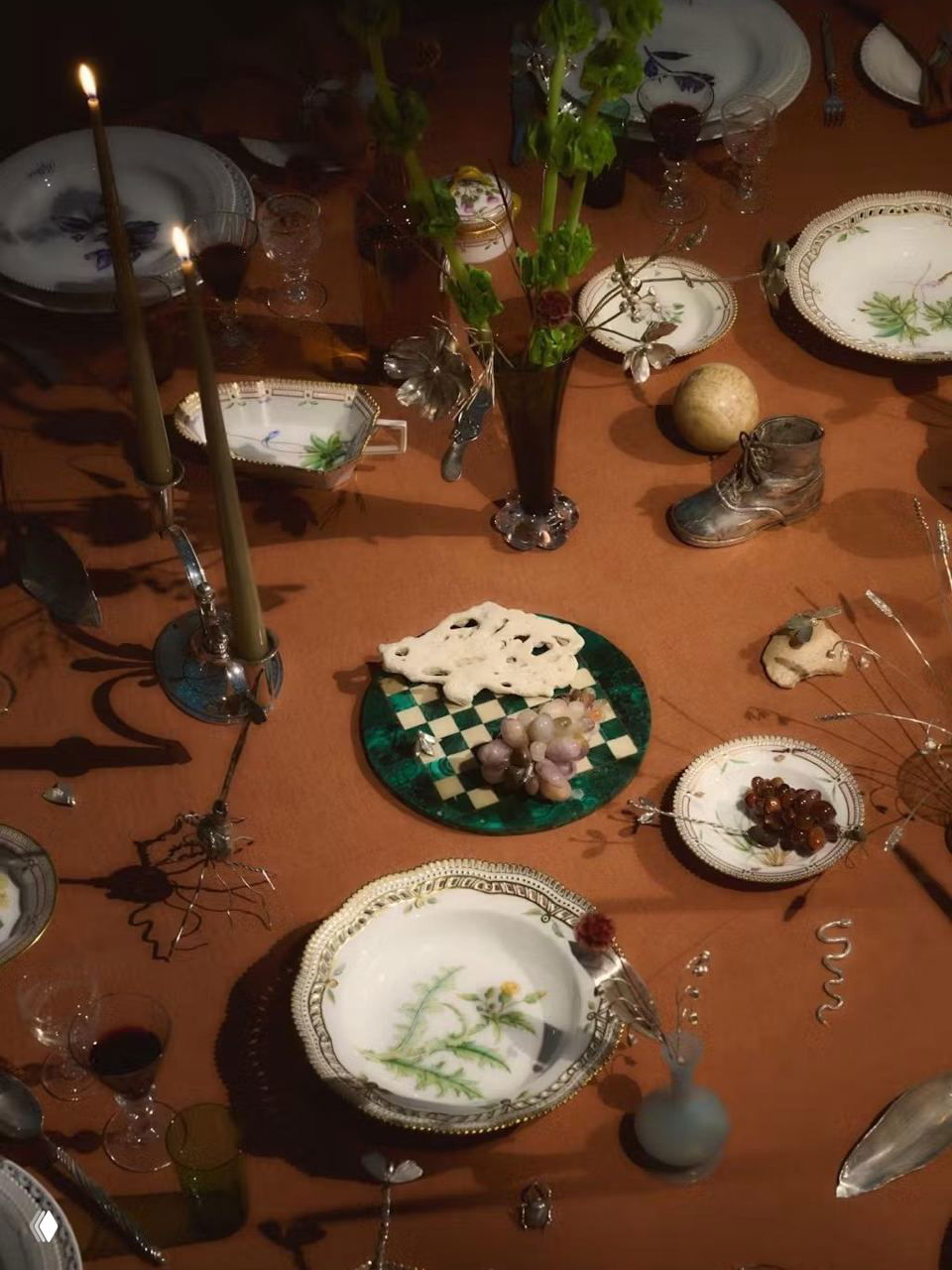 Вид сверху на сервированный стол с подсвечниками, антикварной посудой и мелкими декоративными предметами в художественной композиции для праздника.