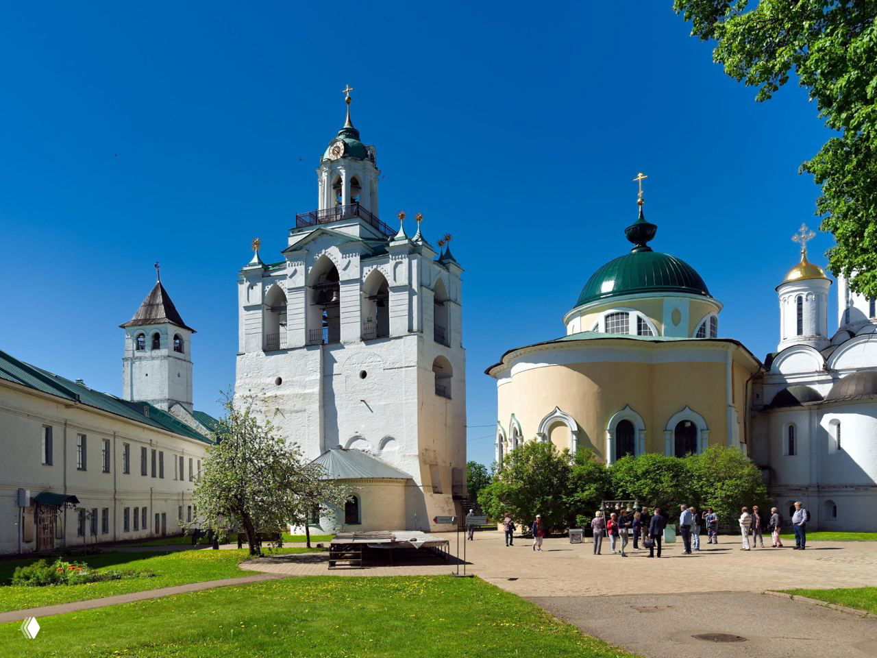 Белая колокольня и купола в архитектурном ансамбле Спасо-Преображенского монастыря, солнечный день, зелёные лужайки и посетители у входа.