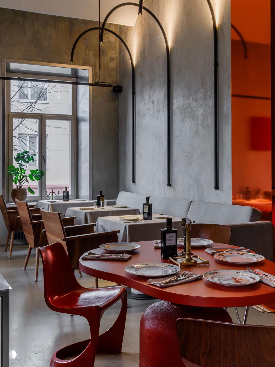 Красный стол и стулья, серые диваны у бетонной стены и дугообразные черные светильники — контраст винтажного и современного в интерьере