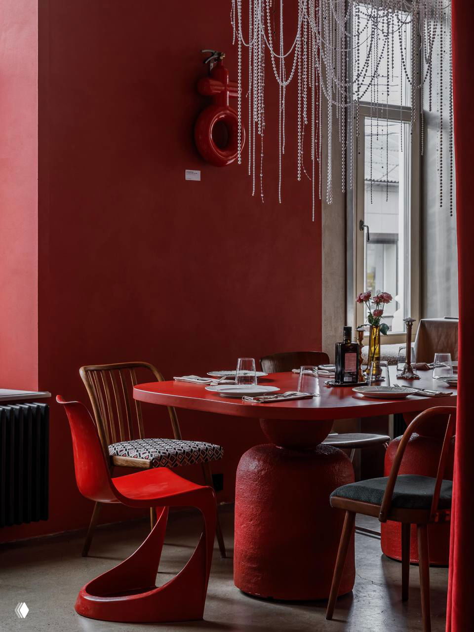 Близкий план сервировки: тарелки, столовые приборы и бутылки оливкового масла на красном столе на фоне окна и серой стены