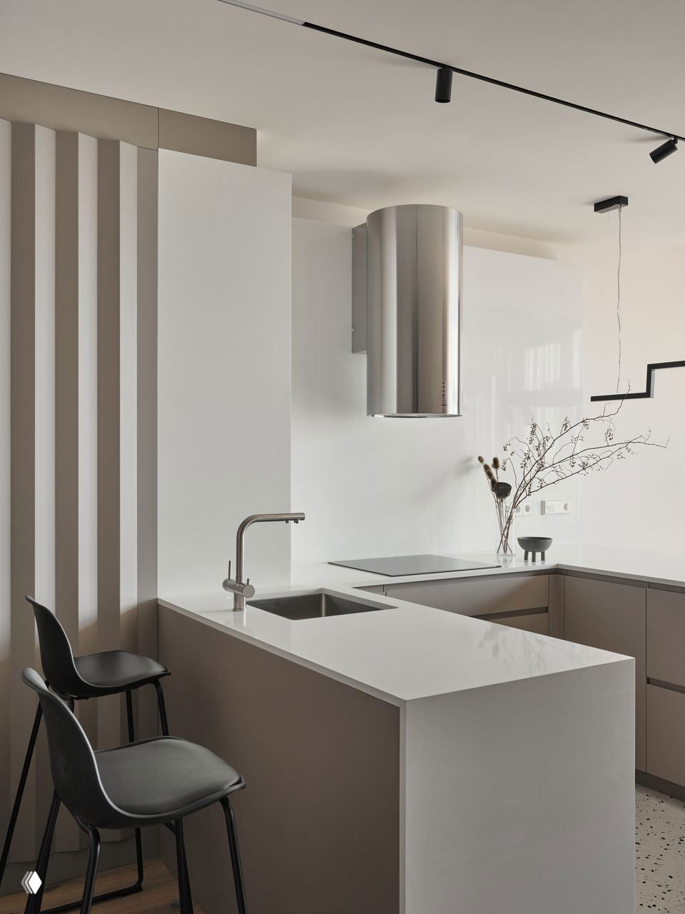 Современный кухонный полуостров с интегрированной мойкой и чистой кубической формой столешницы, нейтральная пастельная палитра и две чёрные барные табуретки.