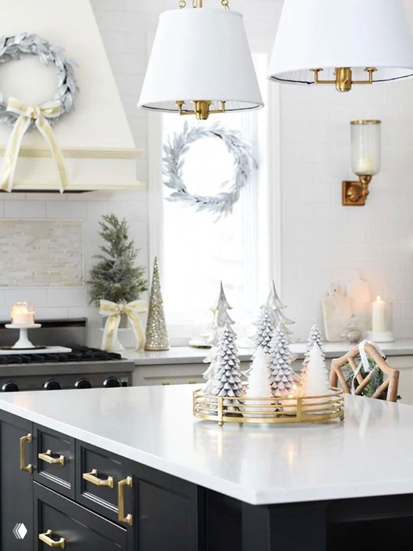 Яркая белая кухня с мраморной столешницей, декоративными керамическими ёлочками и золотыми акцентами на острове — минималистичный праздничный стиль.