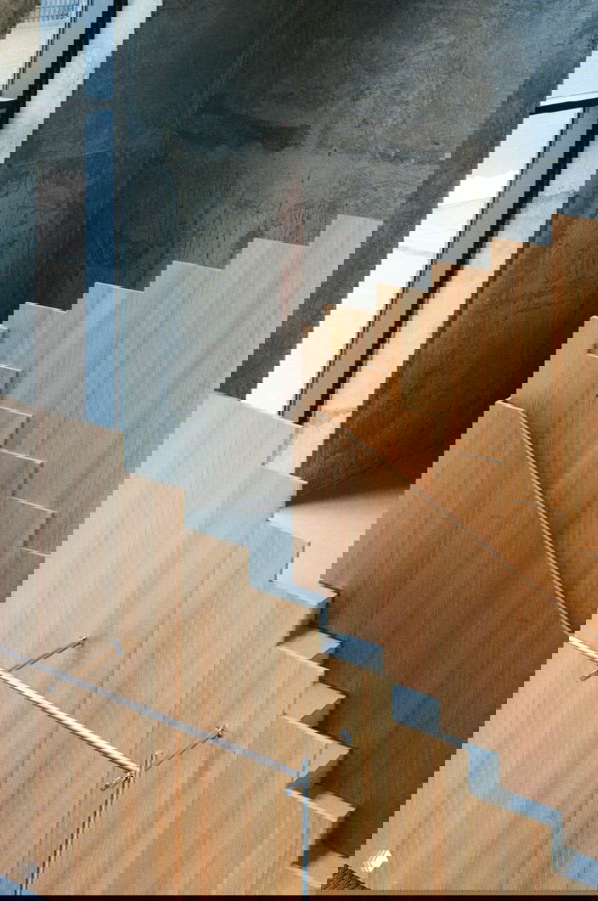 Деревянные щитовые ограждения лестницы из лиственницы на фоне открытого бетона — ступенчатая композиция и естественная фактура в пространстве бистро.