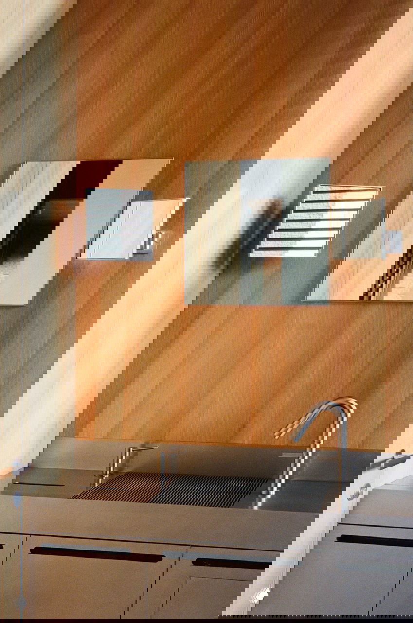 Компактная мойка с нержавеющей столешницей на фоне панелей из лиственницы; аккуратные бытовые детали и отражения в сервисной зоне бистро.